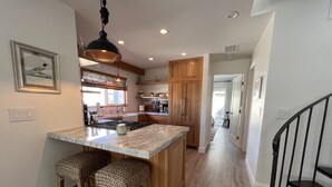 A modern kitchen with a central island, wooden cabinets, and a hanging light fixture. - Seahorse Cottage Luxe (Oxnard)