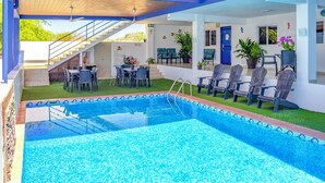 A swimming pool with a tiled deck, outdoor seating, and a staircase leading to an upper level.