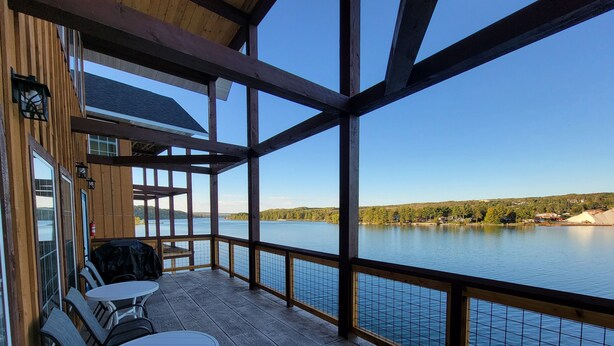 A covered deck with a table and chairs, overlooking a lake with a distant shoreline. - Trailside Fun River Cabin 21B (Houghton)
