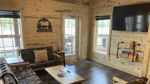 A cozy log cabin interior with a sofa set, a coffee table, and a TV mounted on the wall. - Trailside Fun River Cabin 21B (Houghton)