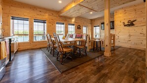 A spacious wooden cabin with a large dining table, multiple chairs, and a kitchen area. - Trailside Fun River Cabin 21B (Houghton)
