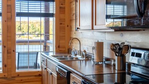 A kitchen with wooden cabinets, a stainless steel sink, and a microwave. - Trailside Fun River Cabin 21B (Houghton)