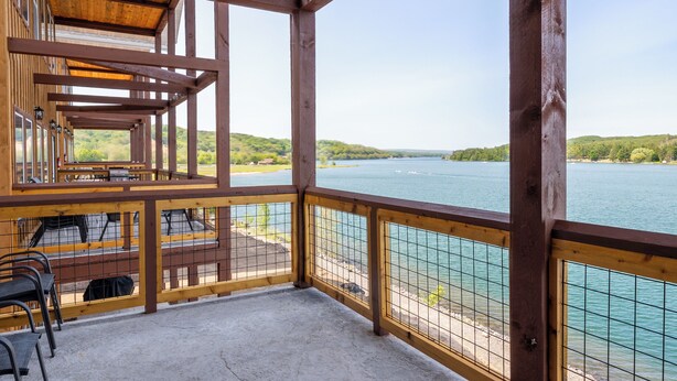 A wooden deck with a view of a lake and hills. - Custom Lakeside Balcony Cabin 20B (Houghton)