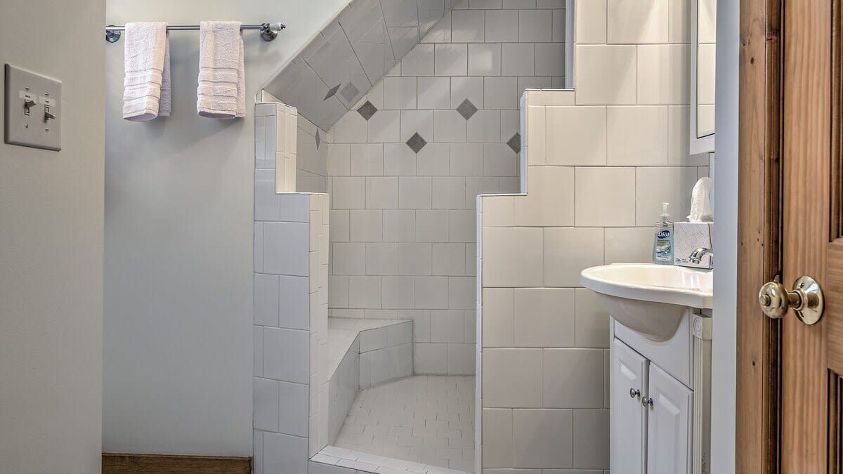 A bathroom with a shower, a sink, and a toilet. There are towels hanging on a rack.
