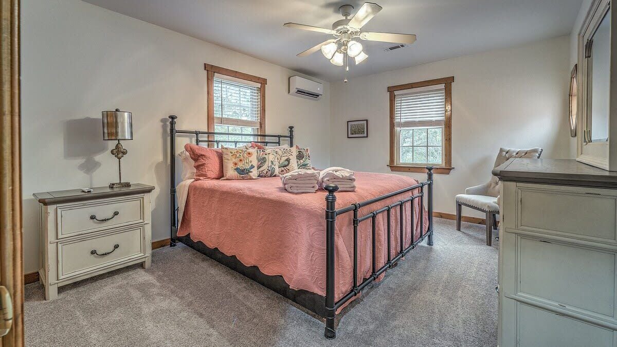 A bedroom with a bed, bedside tables, a dresser, a ceiling fan, and windows.