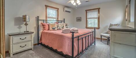 A bedroom with a bed, bedside tables, a dresser, a ceiling fan, and windows.