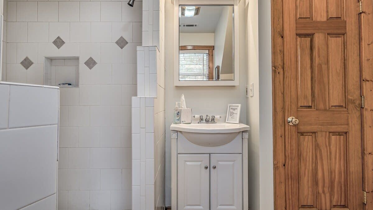 Een badkamer met witte tegels, een houten deur en een wastafel met toiletartikelen.