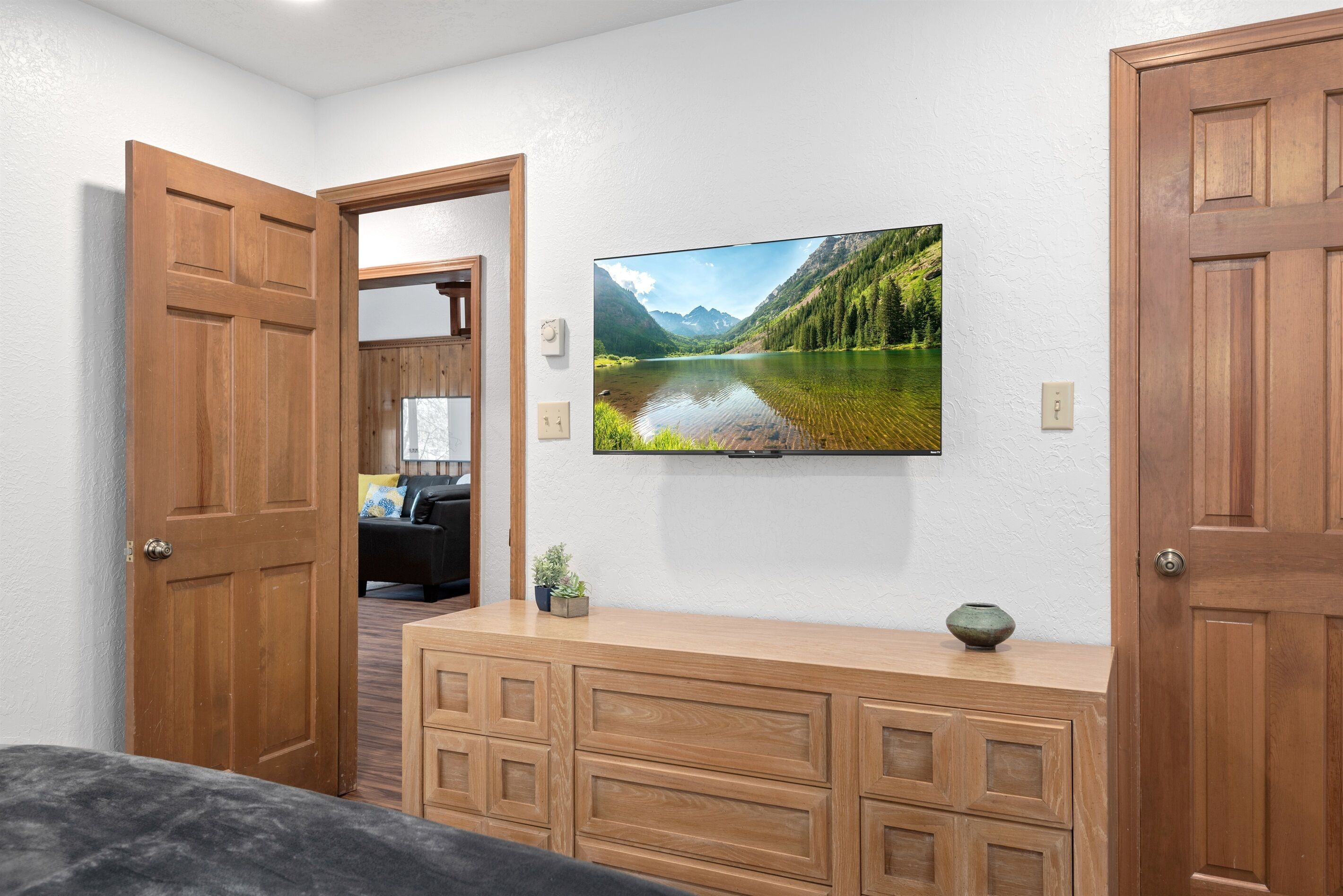Una habitación con un aparador de madera, un televisor en la pared que muestra un paisaje pintoresco y una puerta que da a otra habitación.
