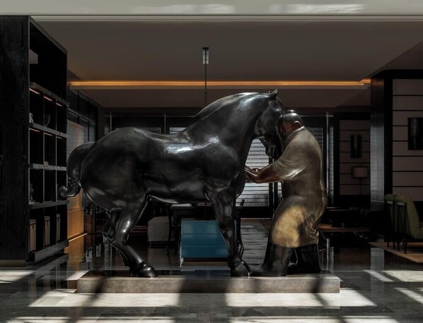 A sculpture of a man and a horse in a modern interior space with a glass floor, metal shelving, and a blue table in the background.
