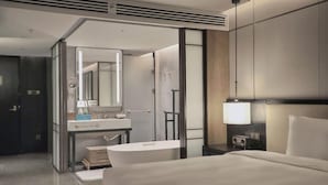 Une chambre d’hôtel moderne dotée d’un grand lit, d’une salle de bain avec baignoire, d’une coiffeuse avec miroir et d’une table de chevet avec une lampe.