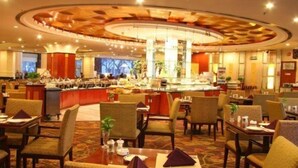 Un hall d’hôtel doté d’un bar central, de plusieurs espaces aménagés pour s’asseoir et offrant une vue sur l’extérieur grâce à de grandes fenêtres.