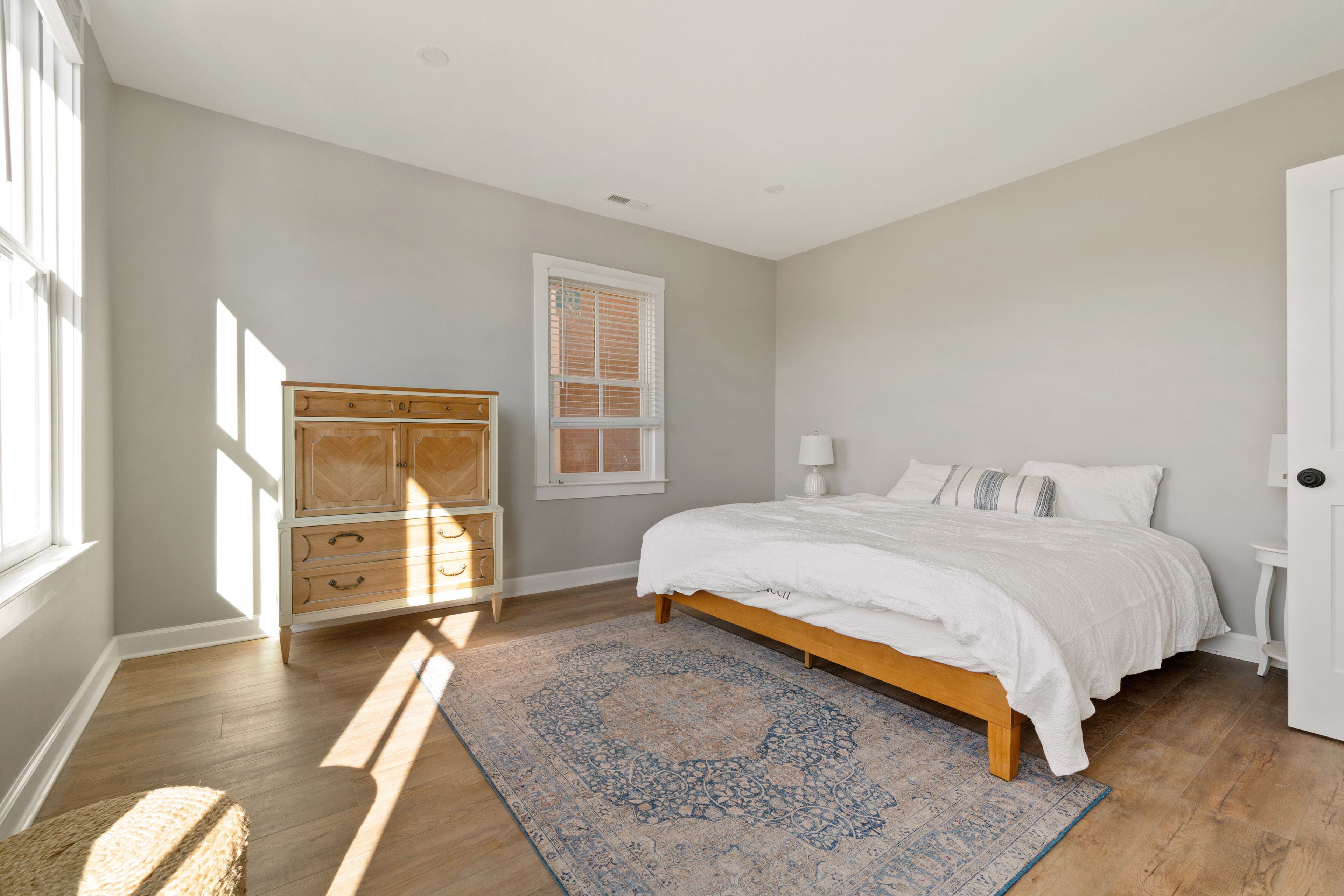 Une chambre à coucher avec un lit, une commode en bois, une fenêtre et un tapis à motifs.