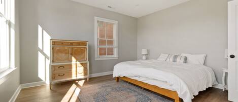 Une chambre à coucher avec un lit, une commode en bois, une fenêtre et un tapis à motifs.