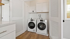 Een kleine wasruimte met twee voorladers, een wit kastje erboven en een houten plank.