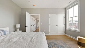 Een slaapkamer met een groot bed, een nachtkastje, een lamp, een kamerbreed tapijt met dessin en zicht door een open deur op een gang.