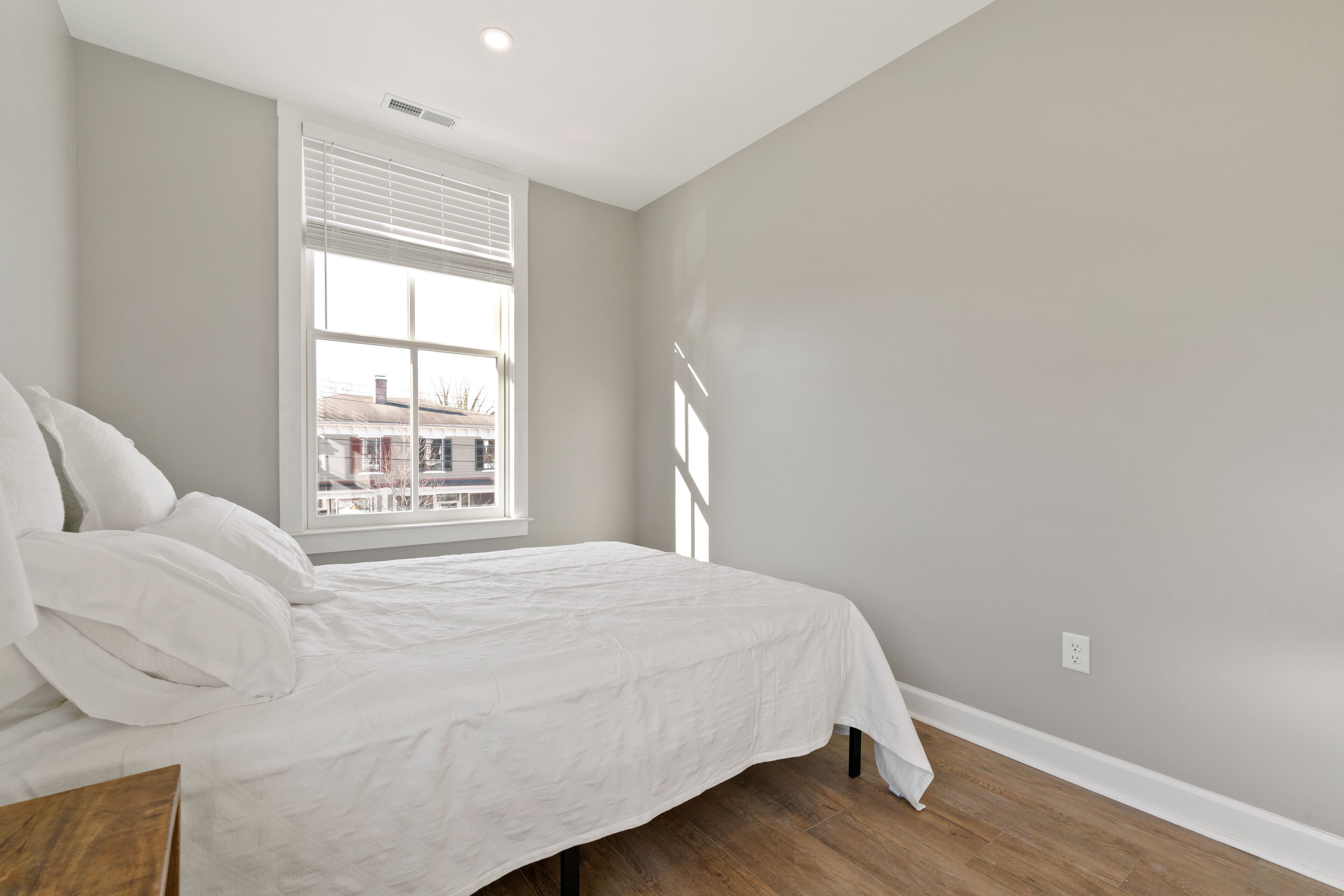 A bedroom with a bed, a window, and a view of buildings outside.