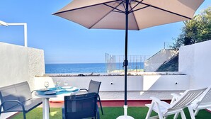 Une terrasse avec une table, des chaises et un parasol, d’où l’on a une vue sur la mer.