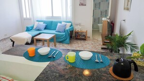Un salon comprenant un canapé, une table basse, une table à manger avec couverts et une bouilloire.