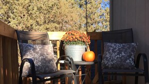 Una terraza de madera con dos sillas y una mesa, un balde de metal con flores y una calabaza.