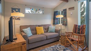 Una sala de estar acogedora con un sofá, un sillón de balancín de madera, una lámpara y una mesita.