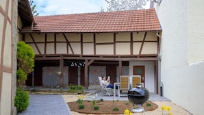 A courtyard with a tiled roof, a grill, and a garden with flowers and plants.