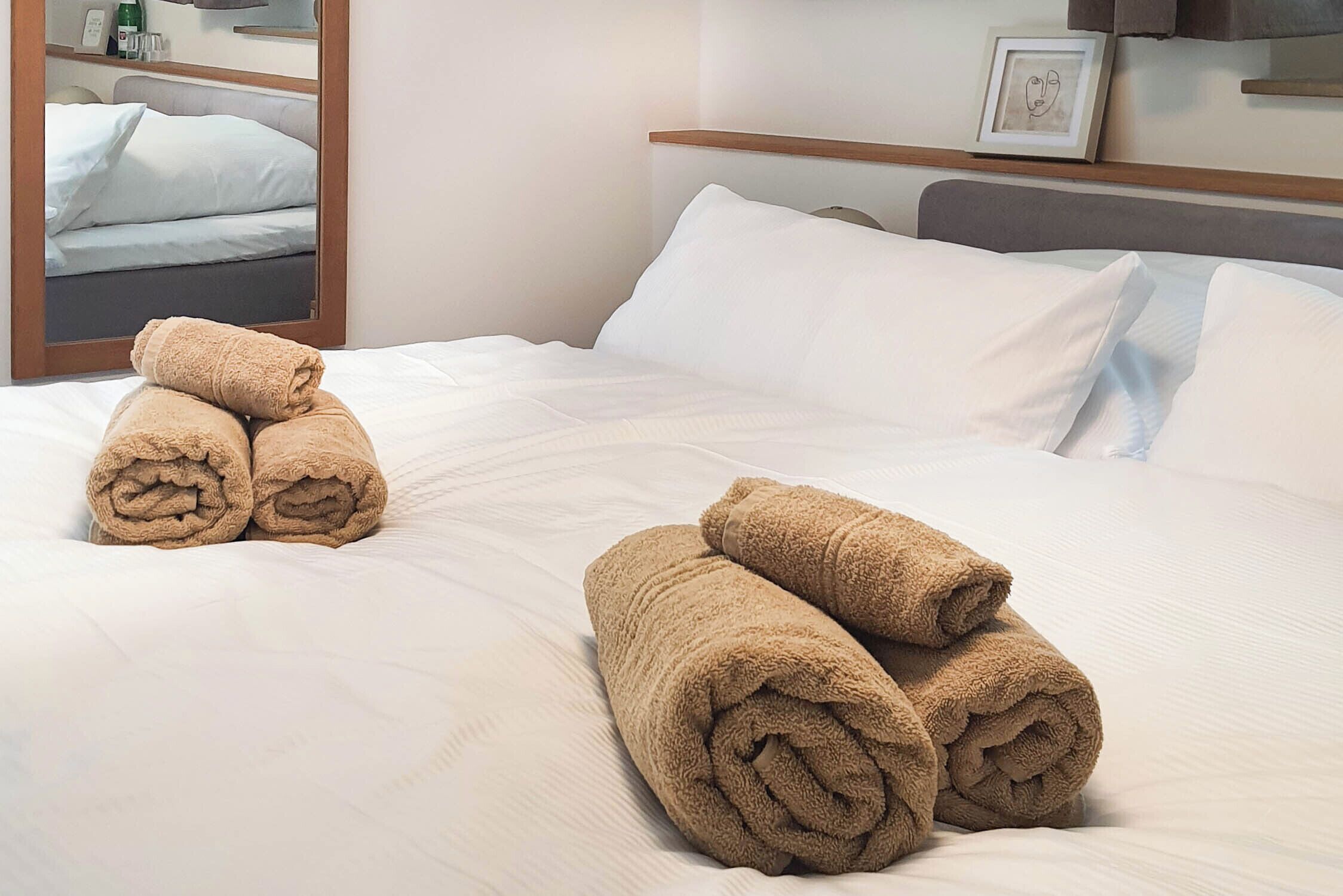 A neatly made bed with rolled towels, a wooden headboard, and a framed picture on the wall.