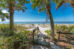 A wooden pathway leading to a beach with palm trees and sandy terrain. - The Manatee House; Unique Beachfront Home & Picturesque Sunsets! (Englewood)