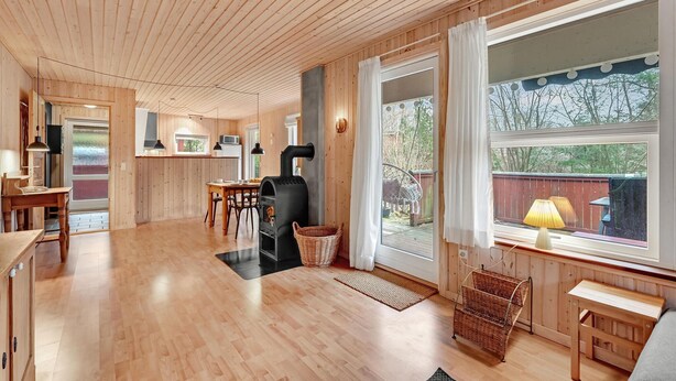 Ein geräumiges Zimmer mit Holzböden, einem Essbereich, einem Kamin und großen Fenstern mit Blick ins Freie.