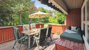 Eine Holzterrasse mit Tisch und Stühlen, einer Hängematte und einer Couch mit Kissen.