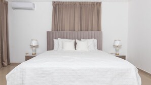 A neatly made bed with a white duvet, a grey headboard, and two bedside lamps. - Beautiful villa in Santo Domingo is  (Santo Domingo Este)