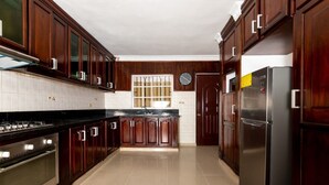 A kitchen with dark wooden cabinets, a stainless steel refrigerator, and a tiled backsplash. - Beautiful villa in Santo Domingo is  (Santo Domingo Este)