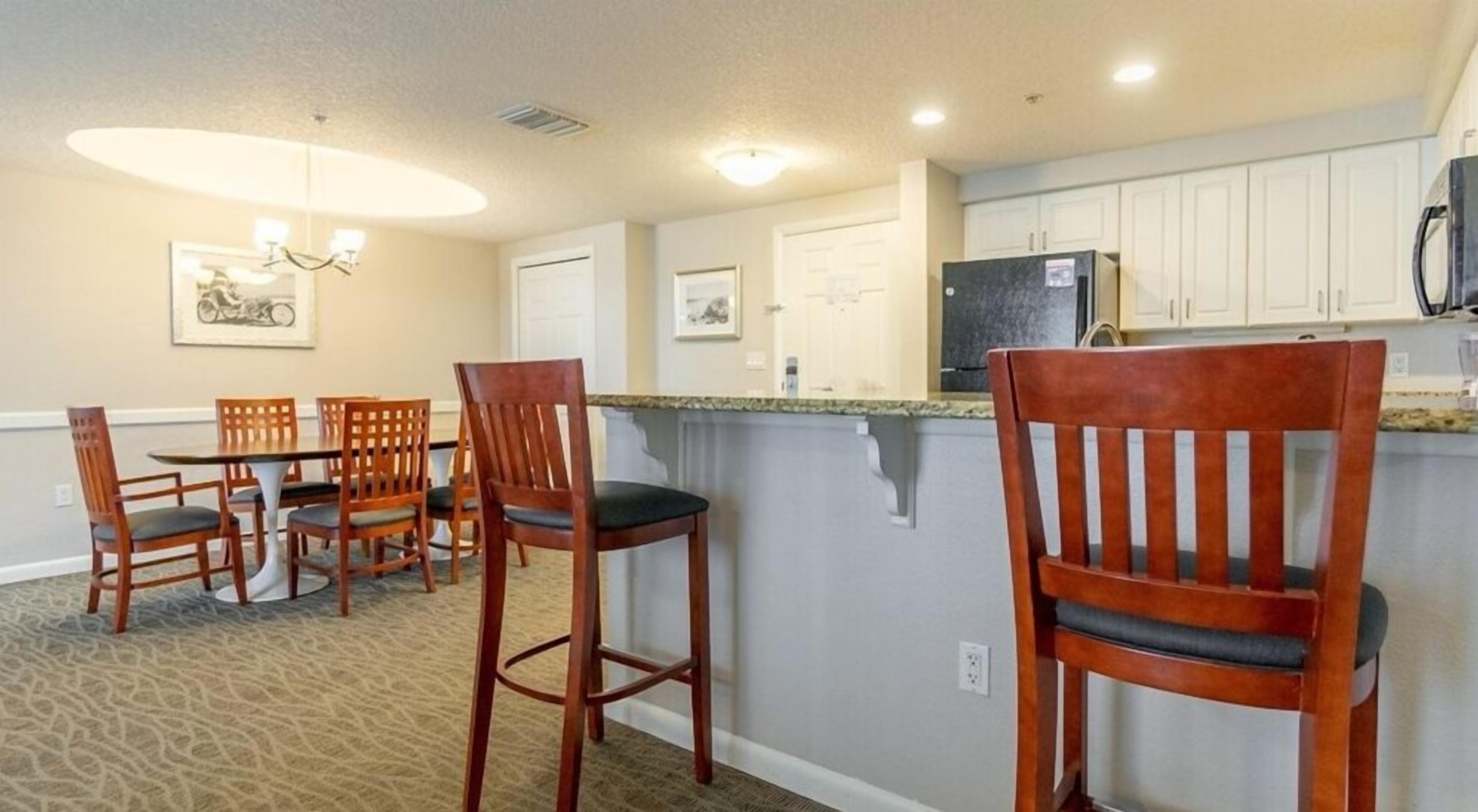 A compact kitchen with a dining area, featuring wooden chairs, a small island, and white cabinets.