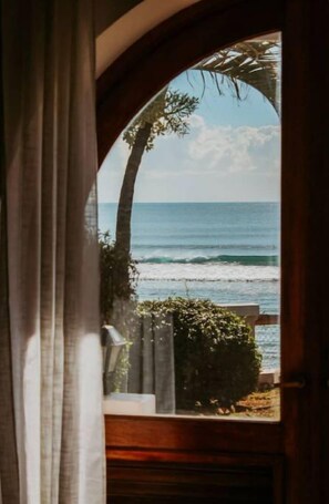 A view through an arched doorway to a beach with waves, a palm tree, and a hedge. - Isla Bonita (Christiansted)