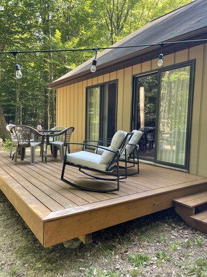 A wooden deck with outdoor furniture, including chairs and a table, and a building with large windows.