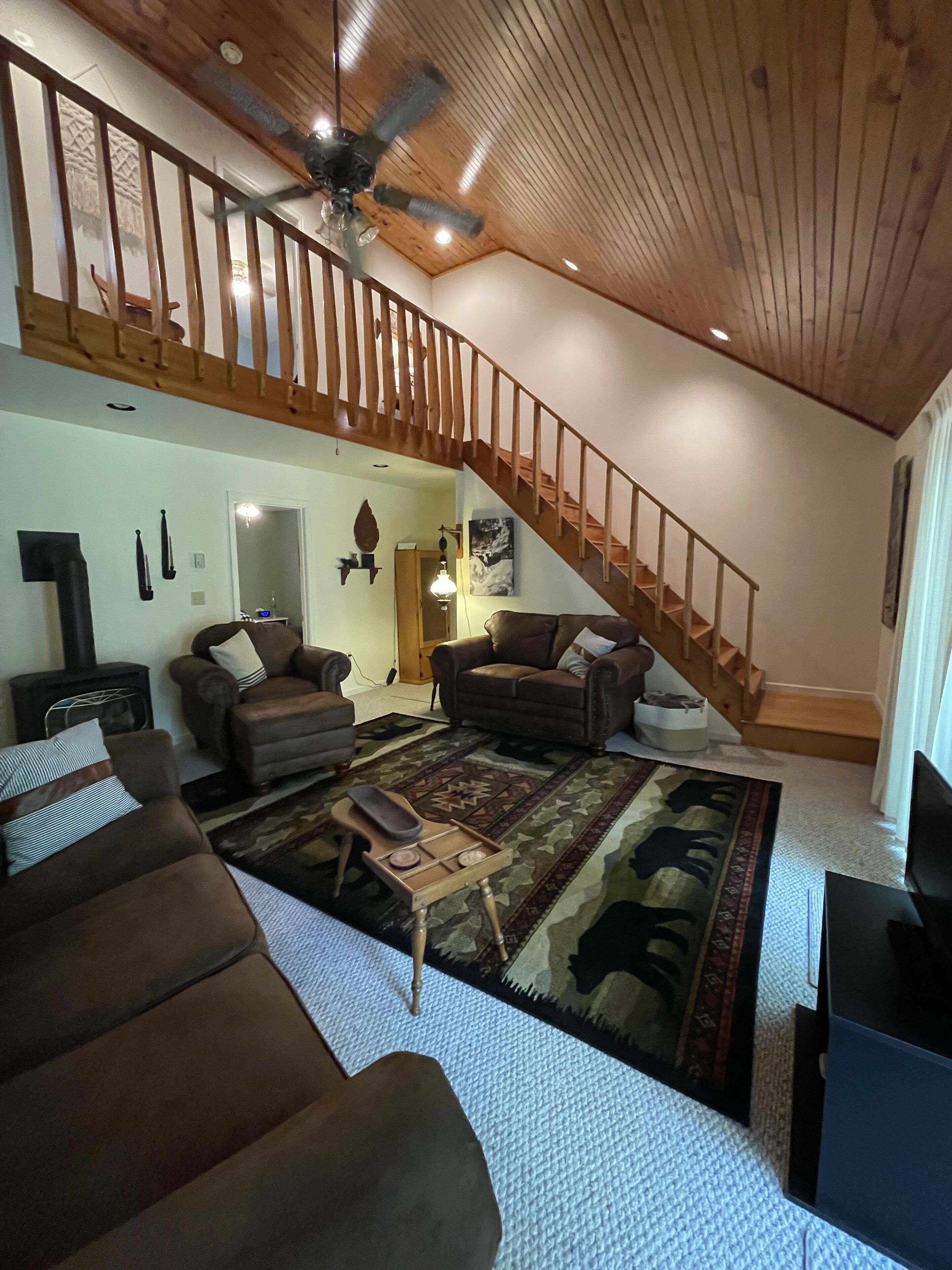 A spacious living room with a high ceiling, a wooden staircase, and a large ceiling fan.