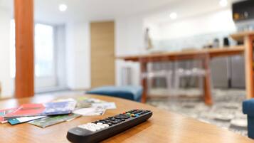 A remote control on a wooden table with magazines and a glass of water.