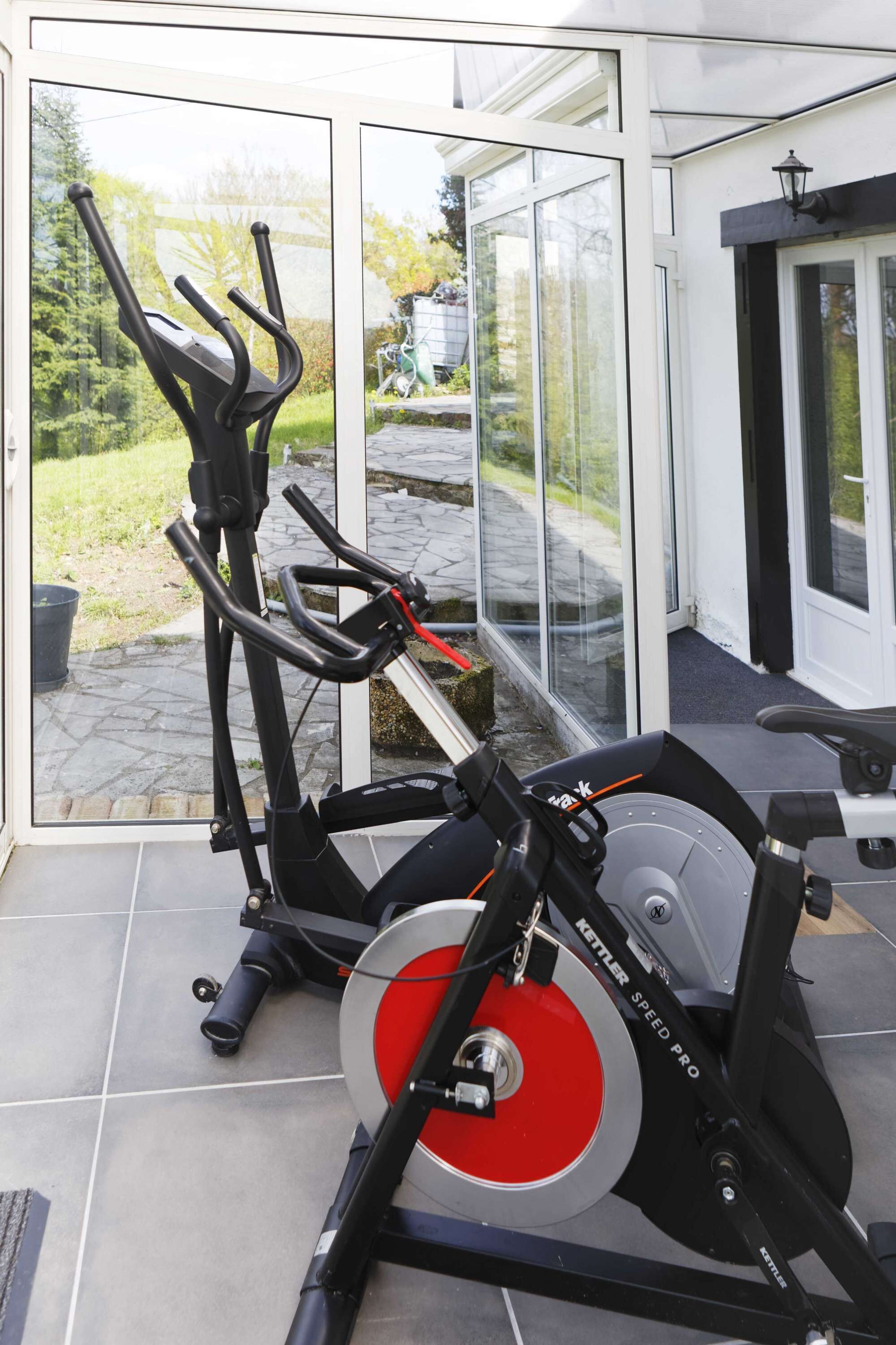 A stationary bike in a room with a glass door leading to a garden.