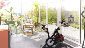 A modern room with a large window, a stationary bike, and a dining area with chairs and a table.