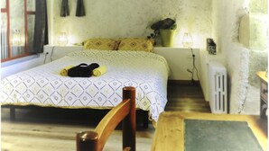 A small, cozy room with a bed, a chair, a table, and a window with curtains.