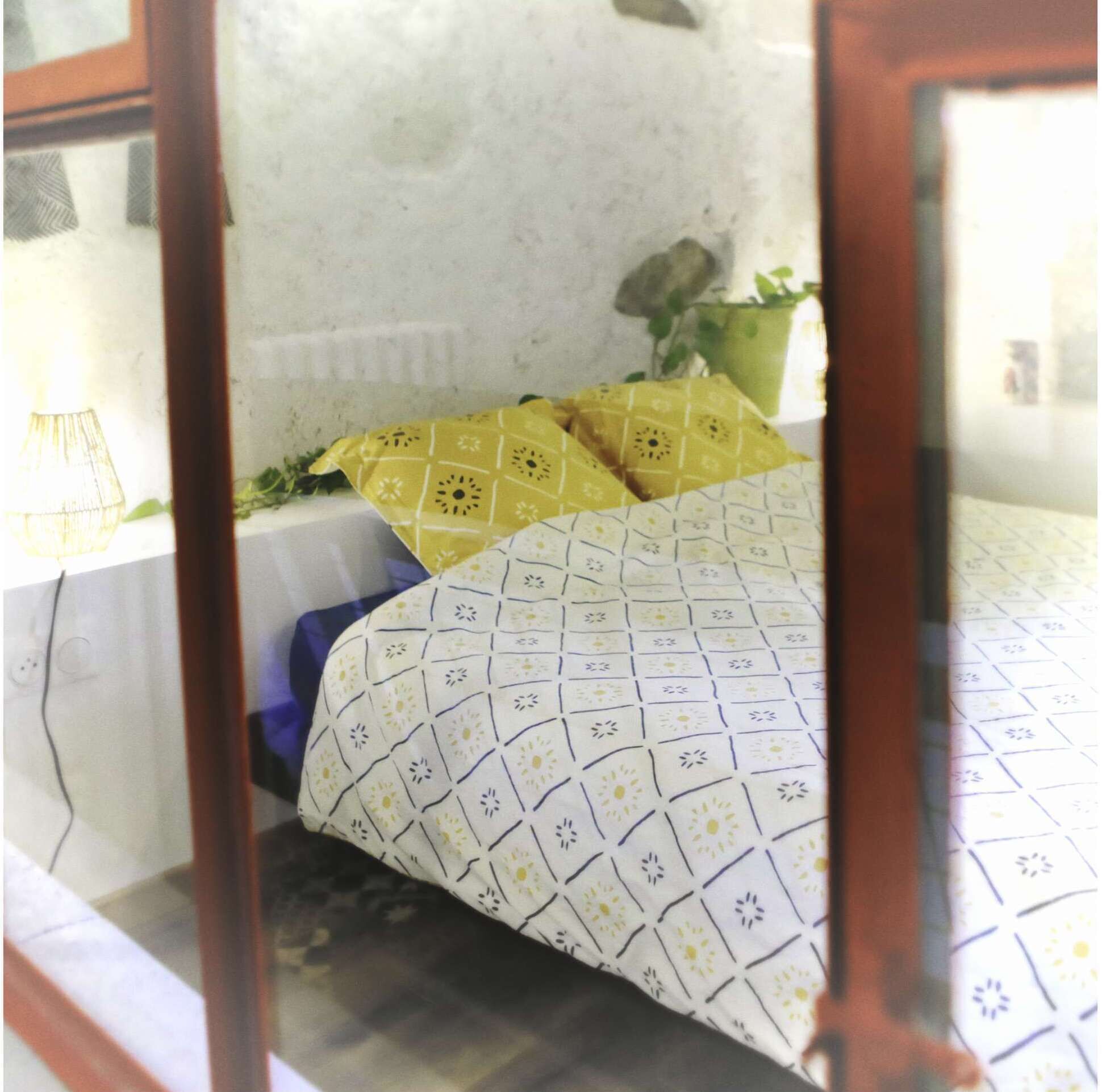A bedroom with a patterned bedspread, a bedside table with a lamp, and a potted plant.