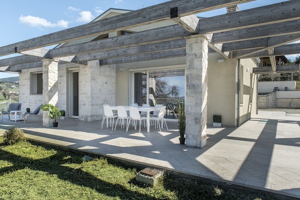 A covered outdoor dining area with stone walls and a wooden pergola.