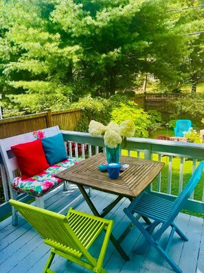 A wooden deck with a white bench, colorful cushions, and a table with a vase of flowers.