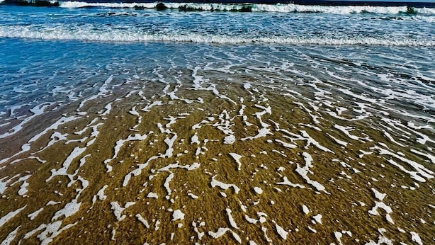 Een strand met helder water en duidelijke zandpatronen.