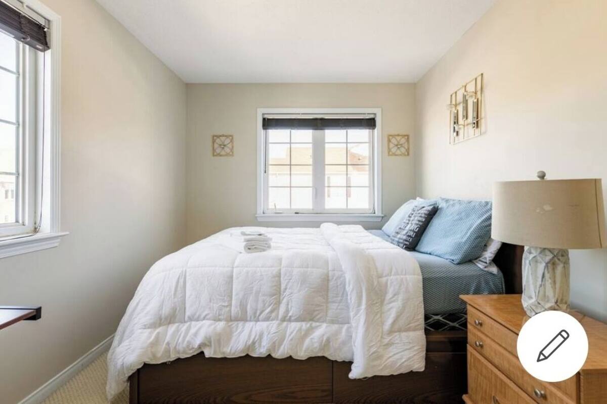 A bedroom with a bed, a nightstand, a lamp, and a window.