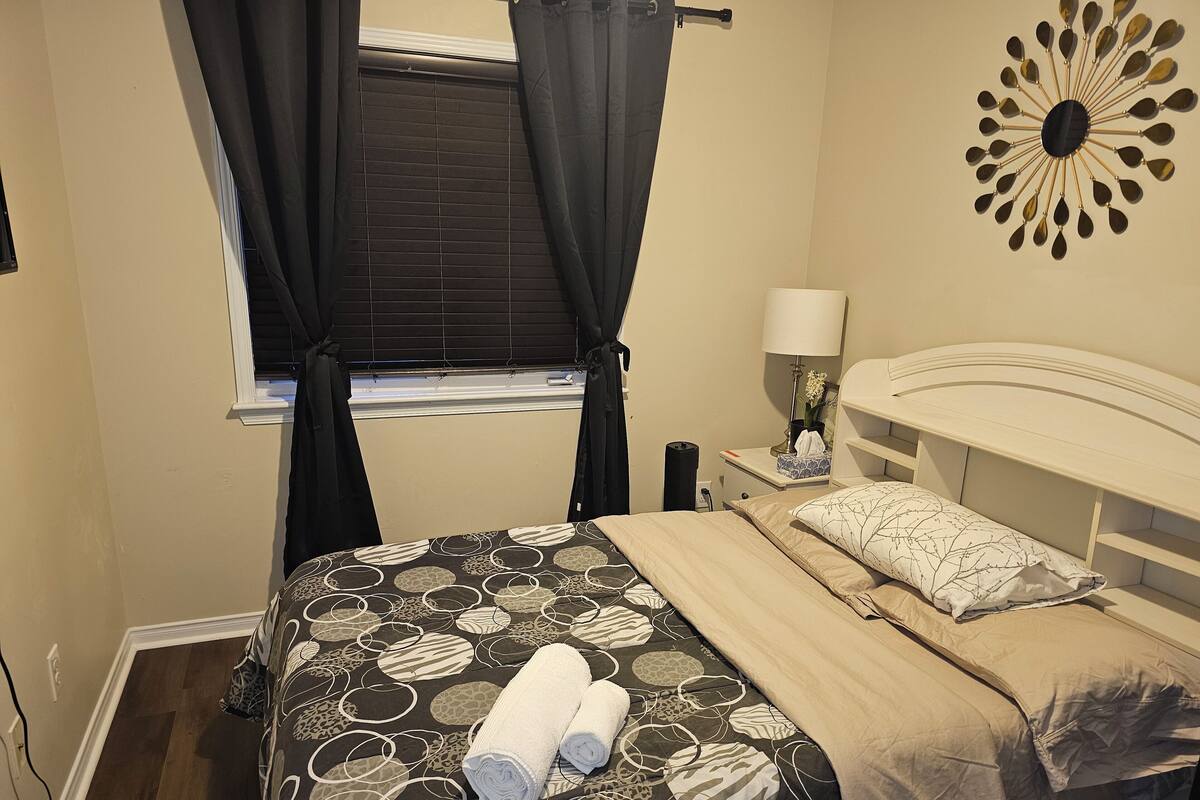 A bedroom with a bed, a nightstand, a lamp, and a window with curtains.