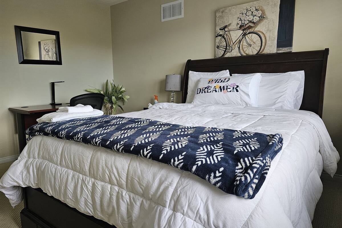 A neatly made bed with a patterned blanket, a headboard, and a pillow with the text "WILD DREAMER".