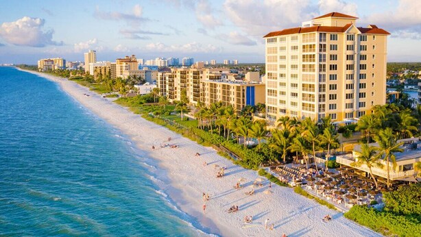 A beachfront hotel with multiple floors, a sandy beach, and palm trees. - Close to Beach heated salt Pool Retreat (Naples)