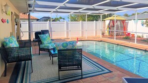 A covered outdoor swimming pool area with lounge chairs and a poolside table. - Close to Beach heated salt Pool Retreat (Naples)