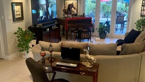 Ett vardagsrum med en tv, ett piano, en soffa och en bärbar dator på ett bord.