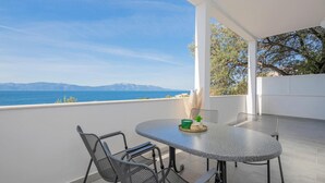 A balcony with a table and chairs, overlooking a body of water and distant mountains.